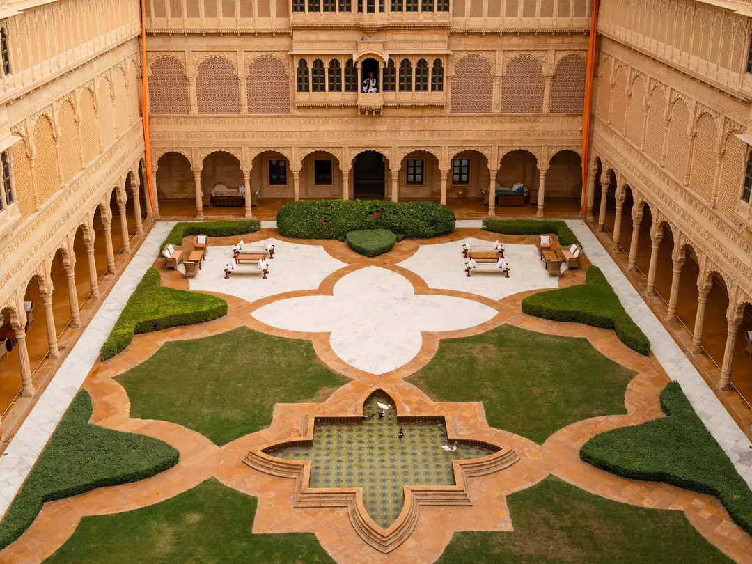 An empty sandstone palace courtyard with lawns, a star-shaped fountain and arcades